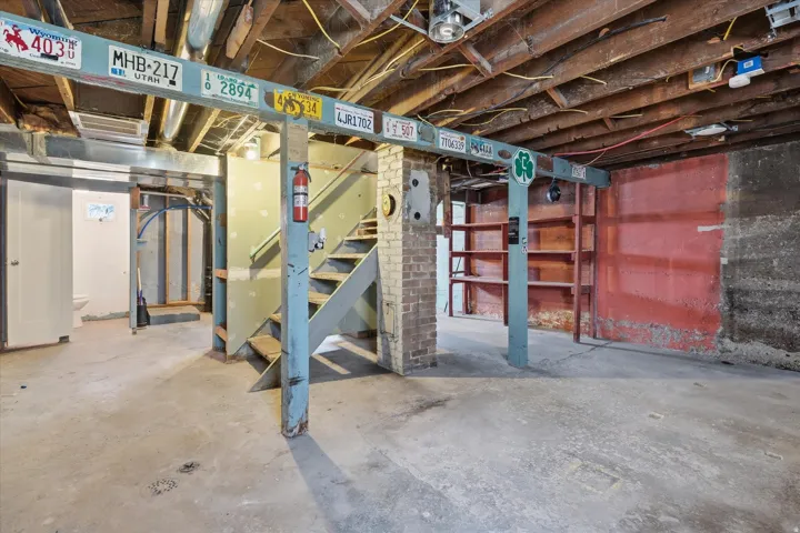 Unfinished basement space with concrete flooring, exposed wood beam ceiling, and interior staircase
