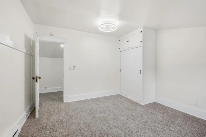 Carpeted room featuring white walls, a built-in closet with sliding doors and upper cabinetry, and a modern ceiling light fixture