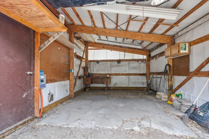 Utility space featuring exposed wood framing, concrete flooring, and overhead lighting