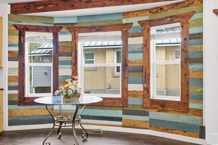 Bay window area featuring a multi-tone wood plank accent wall, three white-framed windows, and dark wood-finish flooring