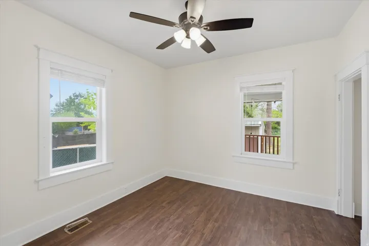 Room with wood-finish flooring, two windows with white trim, and a ceiling fan with integrated lighting