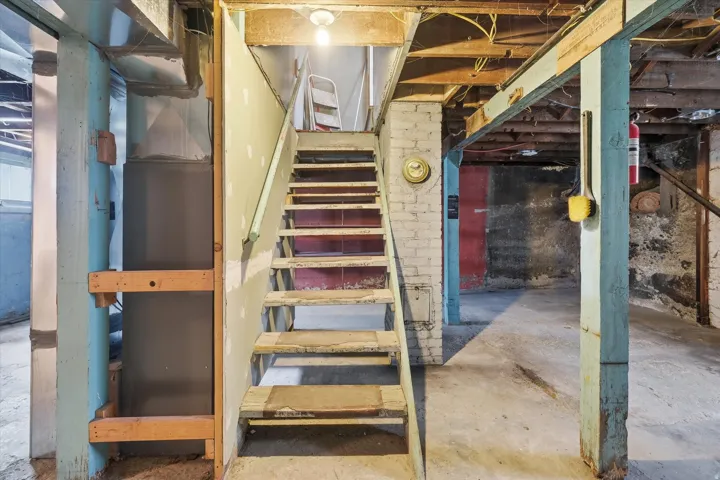 Basement featuring exposed ceiling joists, concrete flooring, and a wooden staircase