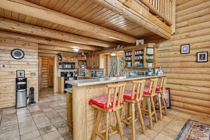 Log cabin interior featuring a kitchen with light wood cabinetry, a breakfast bar with a light-colored countertop, and tiled flooring