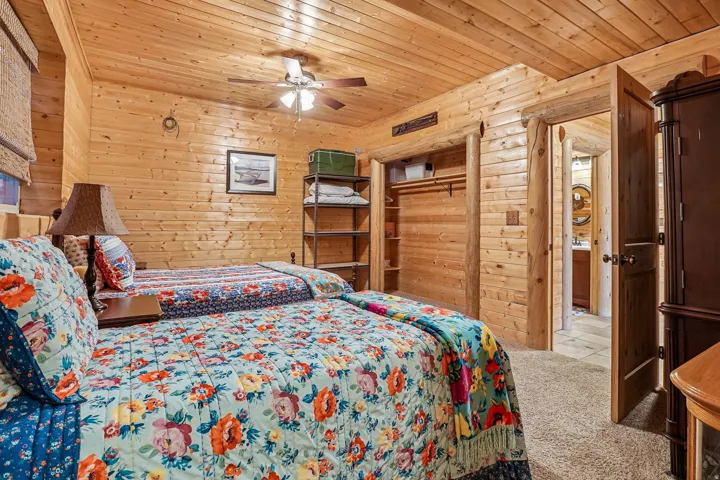 Interior room featuring wood-paneled walls and ceiling, a ceiling fan, plush carpet flooring, a built-in closet with shelving, and a wood-finish door leading to an additional space