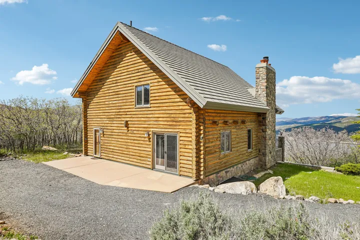 Wood-sided cabin exterior featuring a stone chimney, metal roof, and exposed wood eaves