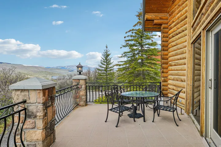 Exterior patio featuring a log cabin facade, stone pillars, wrought iron railing, and large sliding glass doors