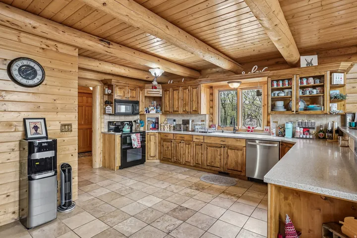 Log cabin kitchen featuring exposed ceiling beams and wood-paneled walls