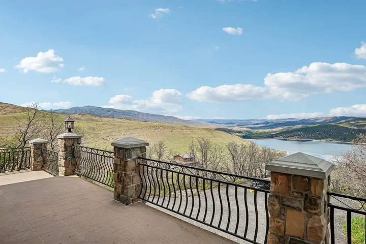 Spacious outdoor patio featuring stone-clad pillars, wrought iron railings, and a vast natural landscape with distant water