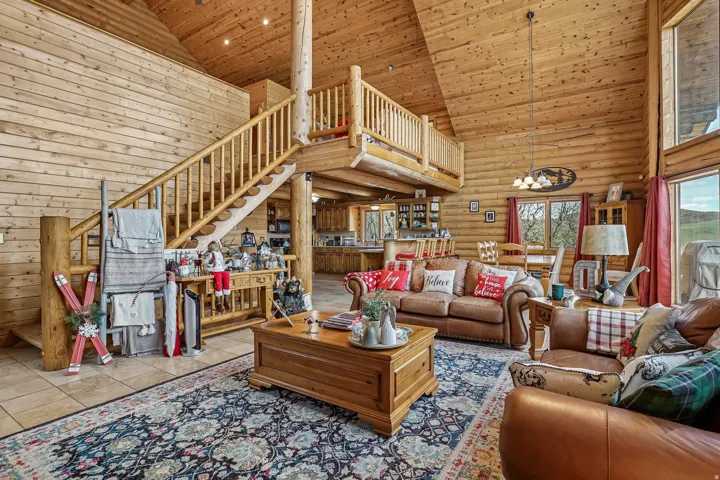 Spacious open-concept living area featuring a vaulted wood-plank ceiling, natural wood walls, and a prominent wood staircase leading to an upper-level balcony