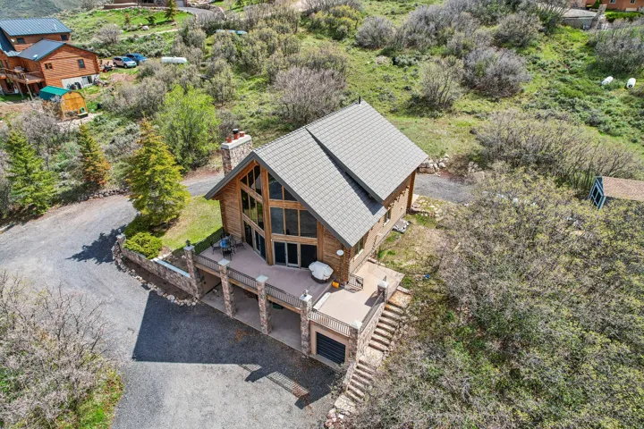 Rustic wood-sided home featuring a prominent A-frame window wall, a stone chimney, a multi-level deck, a stone retaining wall, and a multi-pitched roofline