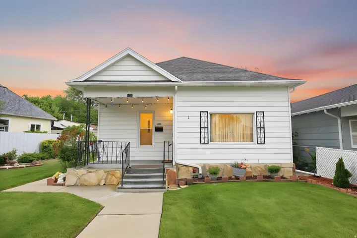 White siding exterior featuring a covered front porch with string lights, dark roof shingles, and a manicured lawn