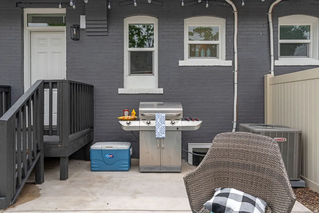Outdoor patio area featuring a concrete surface, dark gray brick exterior, a white panel door, and white-trimmed windows