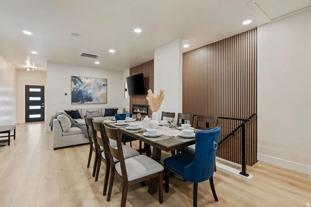 Open-concept living area featuring light wood-finish flooring, recessed lighting, a modern fireplace, and a textured wood-panel accent wall