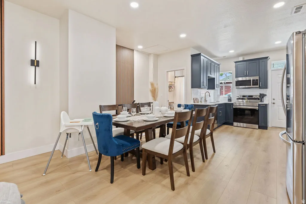 Open-concept dining area featuring wood-finish flooring, recessed lighting, a contemporary wall sconce, and a wood-slat accent wall