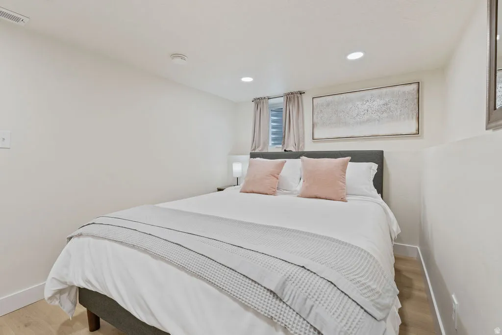 Bedroom featuring recessed lighting, a window with roller blinds, light wood-finish flooring, and crisp white walls