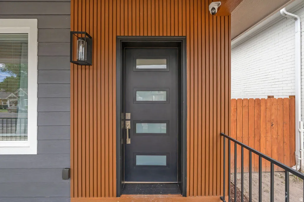 Modern entryway featuring a dark-paneled door with frosted glass inserts, vertical wood-finish siding, and dark gray horizontal siding