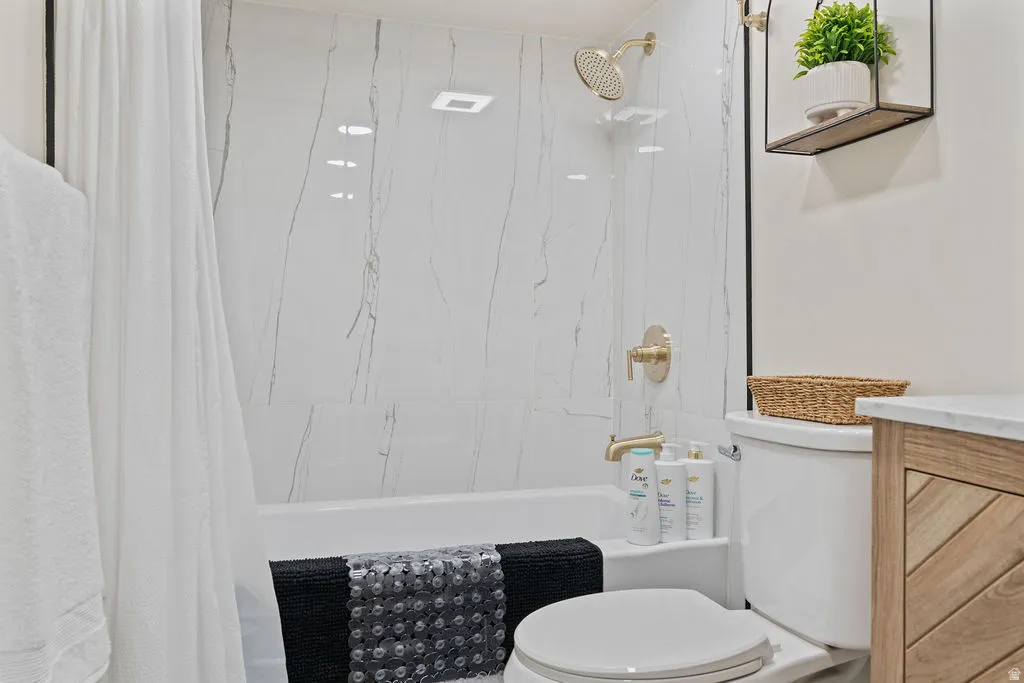 Bathroom featuring a white subway tile tub surround with subtle grey veining, gold-tone shower fixtures, and a white toilet