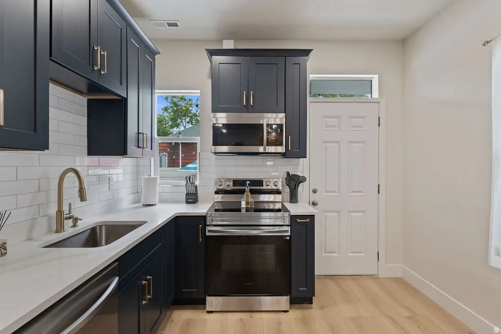 Kitchen featuring dark blue cabinetry, light countertops, subway tile backsplash, stainless steel appliances, and wood-finish flooring
