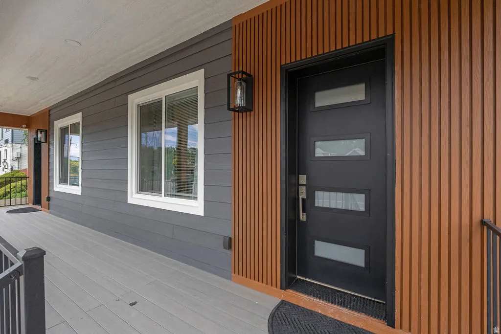 Modern entry featuring a black door with frosted glass panels, vertical wood-finish siding, gray horizontal siding, and a gray-toned porch floor