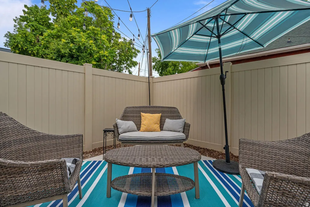 Enclosed patio space featuring a neutral-toned privacy fence, string lighting, and a patterned outdoor rug
