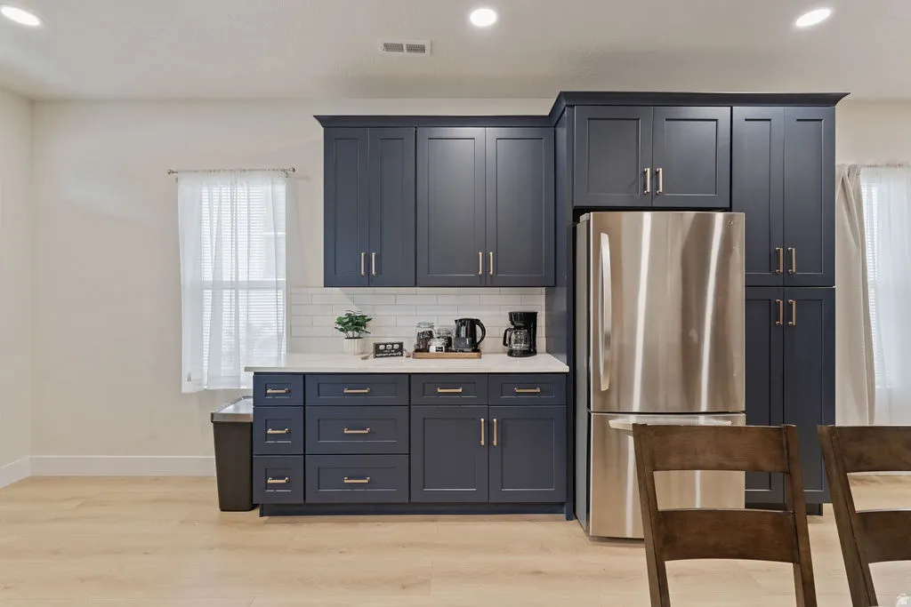 Kitchen featuring dark blue shaker-style cabinetry, stainless steel refrigerator, white subway tile backsplash, and light-toned wood-finish flooring