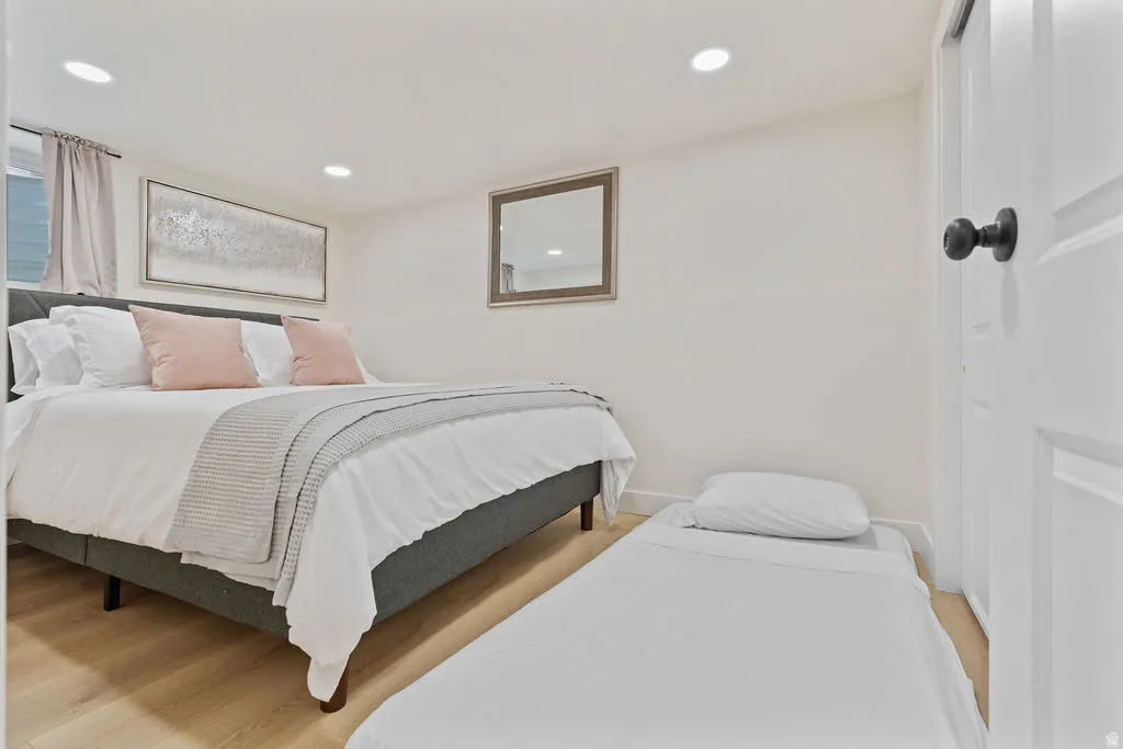 Bedroom featuring light wood-finish flooring, recessed lighting, and a window with light-colored drapes