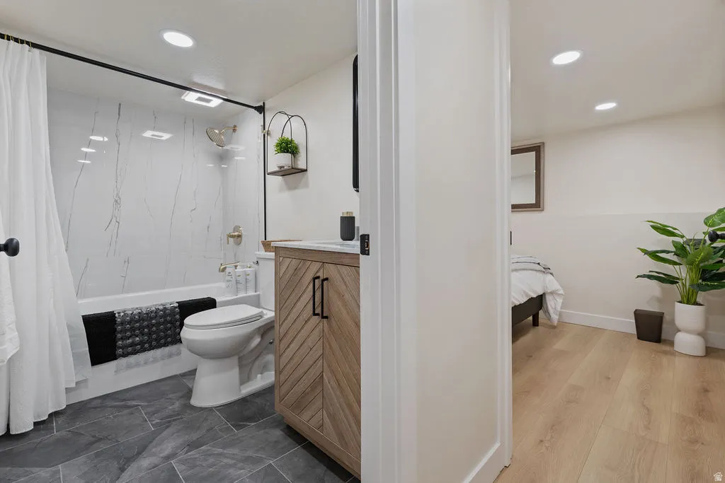Bathroom featuring a bathtub with a marble-look tile surround, a wood-finish vanity with a white countertop, and dark gray floor tiles