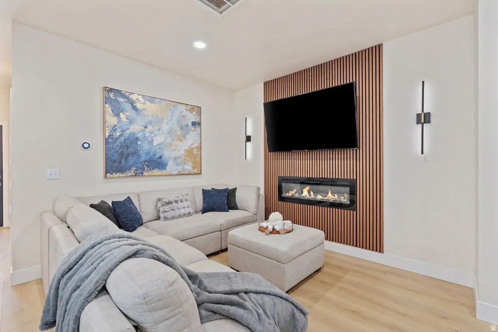 Living area featuring a linear electric fireplace with a wood-slat accent wall, recessed lighting, and light wood-finish flooring