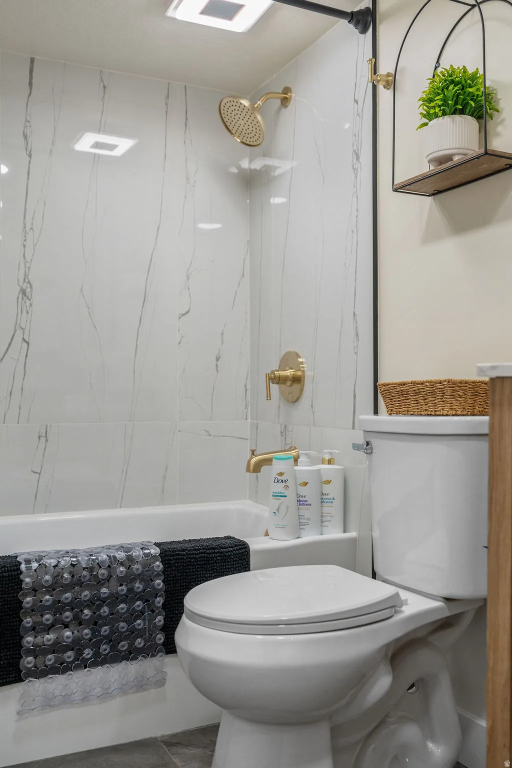 Contemporary bathroom featuring a tub/shower combination with large format marble-look tile surround and gold-finish fixtures