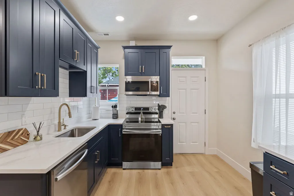 Modern kitchen featuring navy cabinetry with brass hardware, white subway tile backsplash, light wood-finish flooring, and white countertops