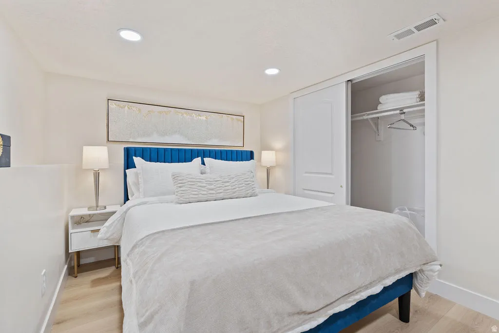 Recessed lighting illuminates this bright room featuring wood-finish flooring, a built-in closet with sliding panel doors, and a wall-mounted overhead vent