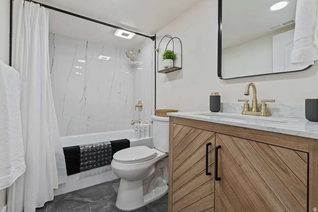 Bathroom featuring a wood-finish vanity with chevron-pattern doors, a white marble-look countertop, and a rectangular undermount sink with brass-finish faucet