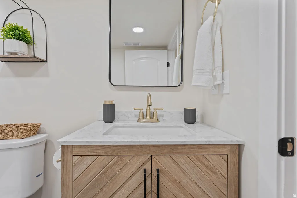 Bathroom vanity featuring a light wood-finish cabinet with chevron-patterned doors, a white countertop, an undermount sink, and a brass-toned faucet