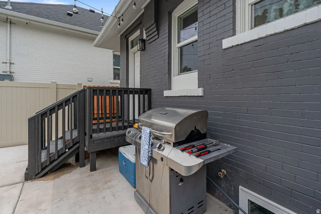 Exterior patio featuring a black-painted wood deck with stairs, a privacy fence, and a gray brick facade with white trim