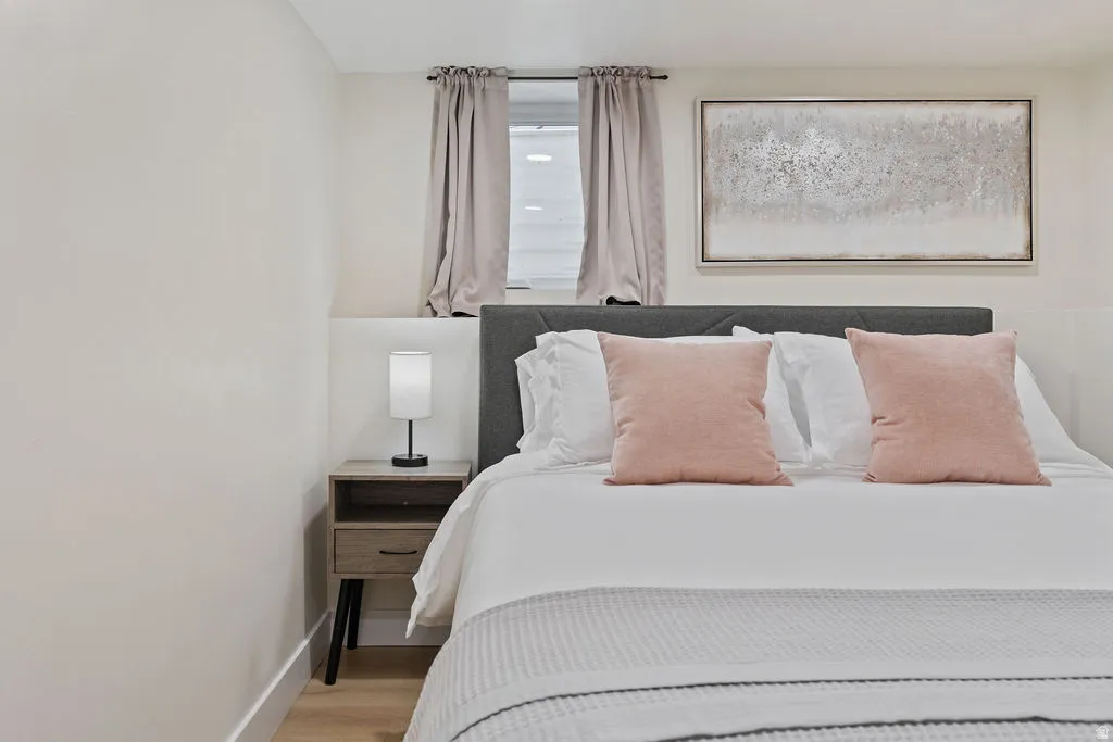 Bedroom featuring a gray upholstered headboard, a window with blinds and drapes, and wood-finish flooring