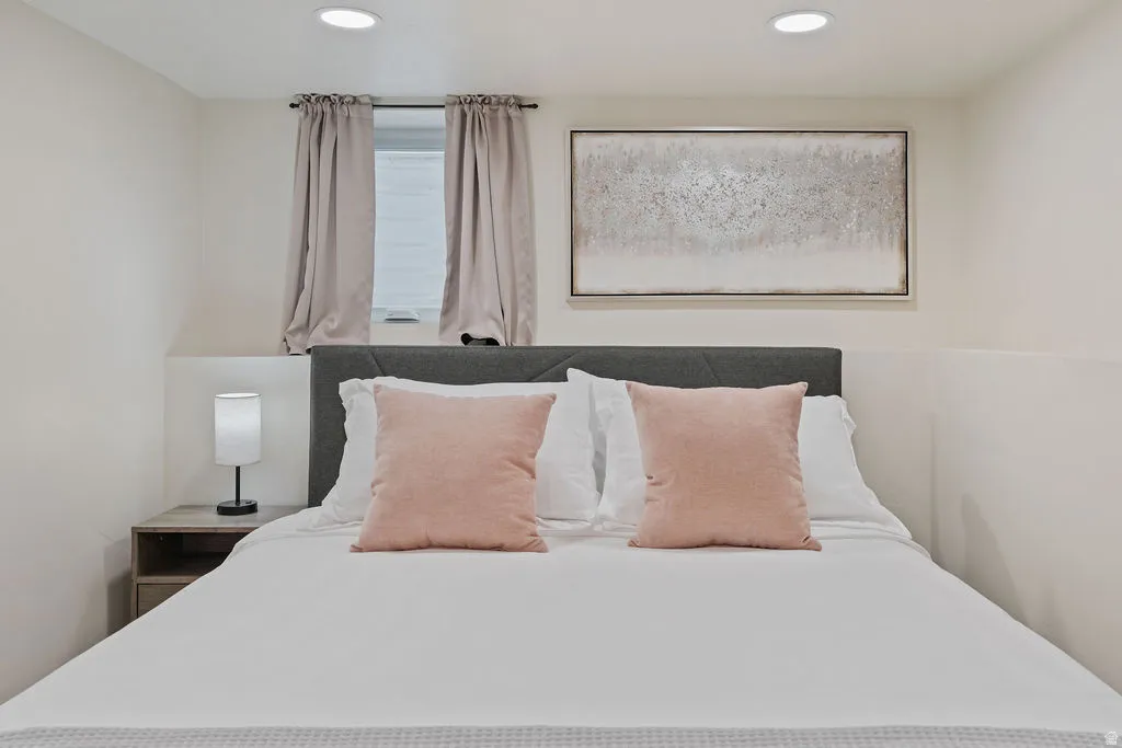Bedroom featuring a window with privacy blinds, recessed ceiling lighting, and a textured wall art piece