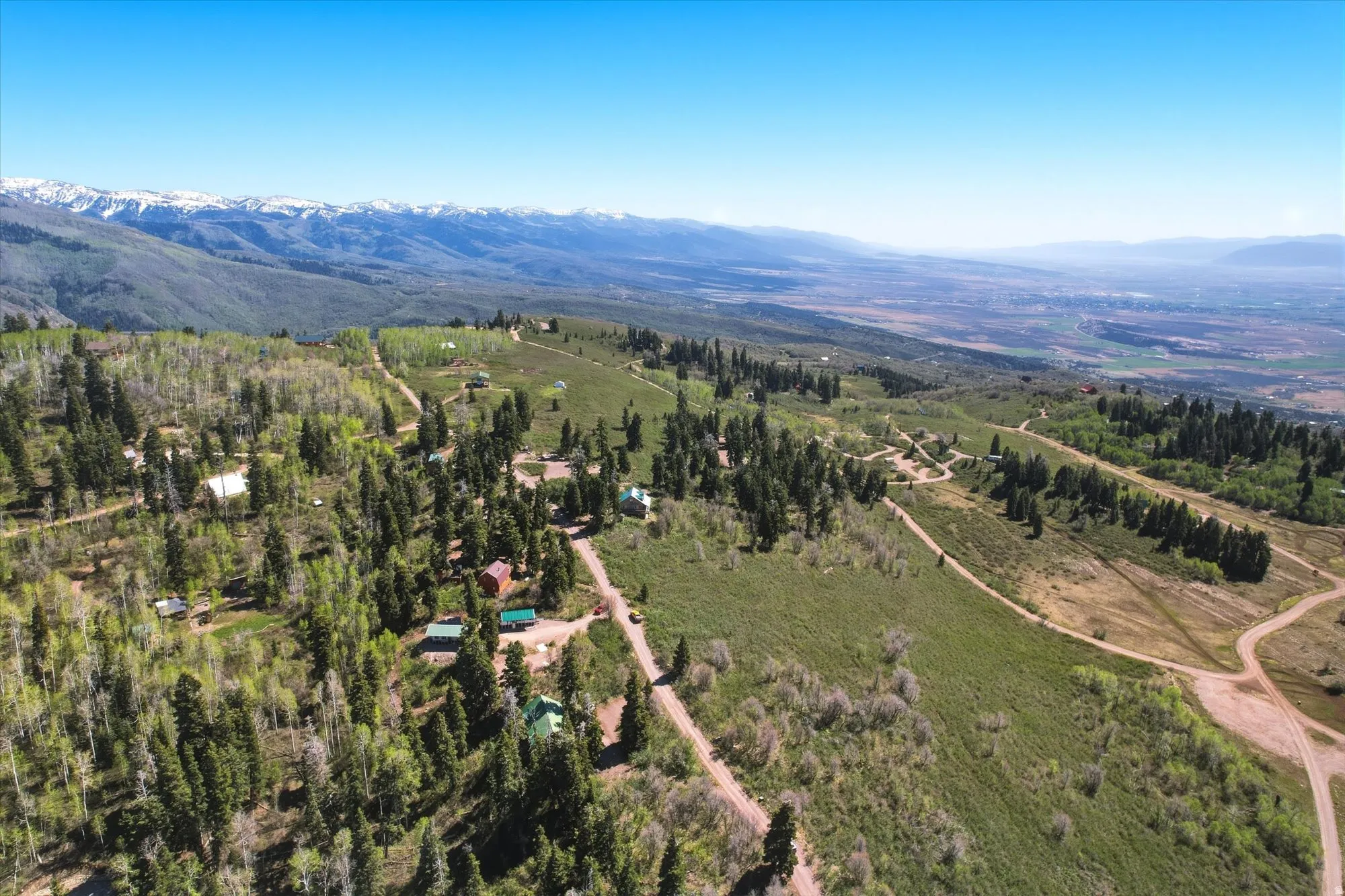 Expansive mountainous terrain with multiple structures, winding dirt roads, a treed landscape, and snow-capped peaks in the distance