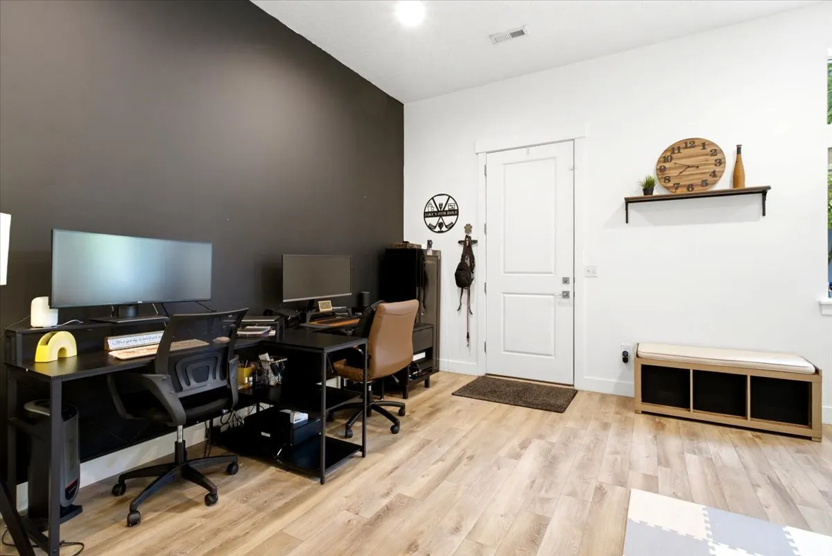 Spacious room with light wood-finish flooring, a white paneled door, and a contrasting dark accent wall