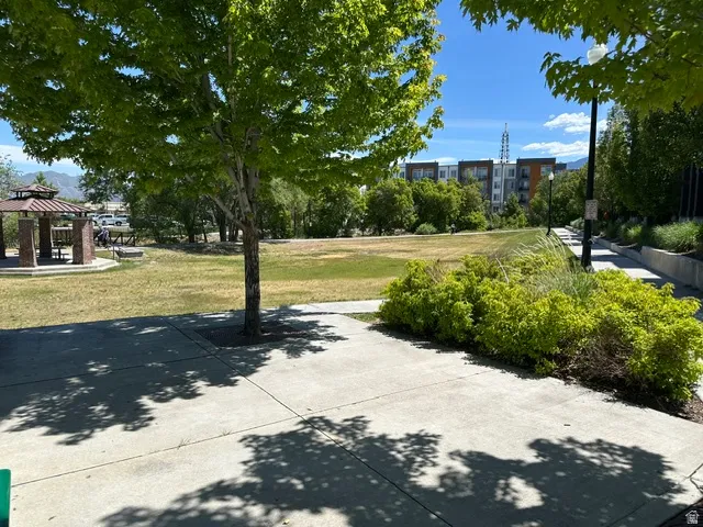 Expansive green space featuring a concrete pathway, mature trees, a gazebo, and distant multi-story buildings