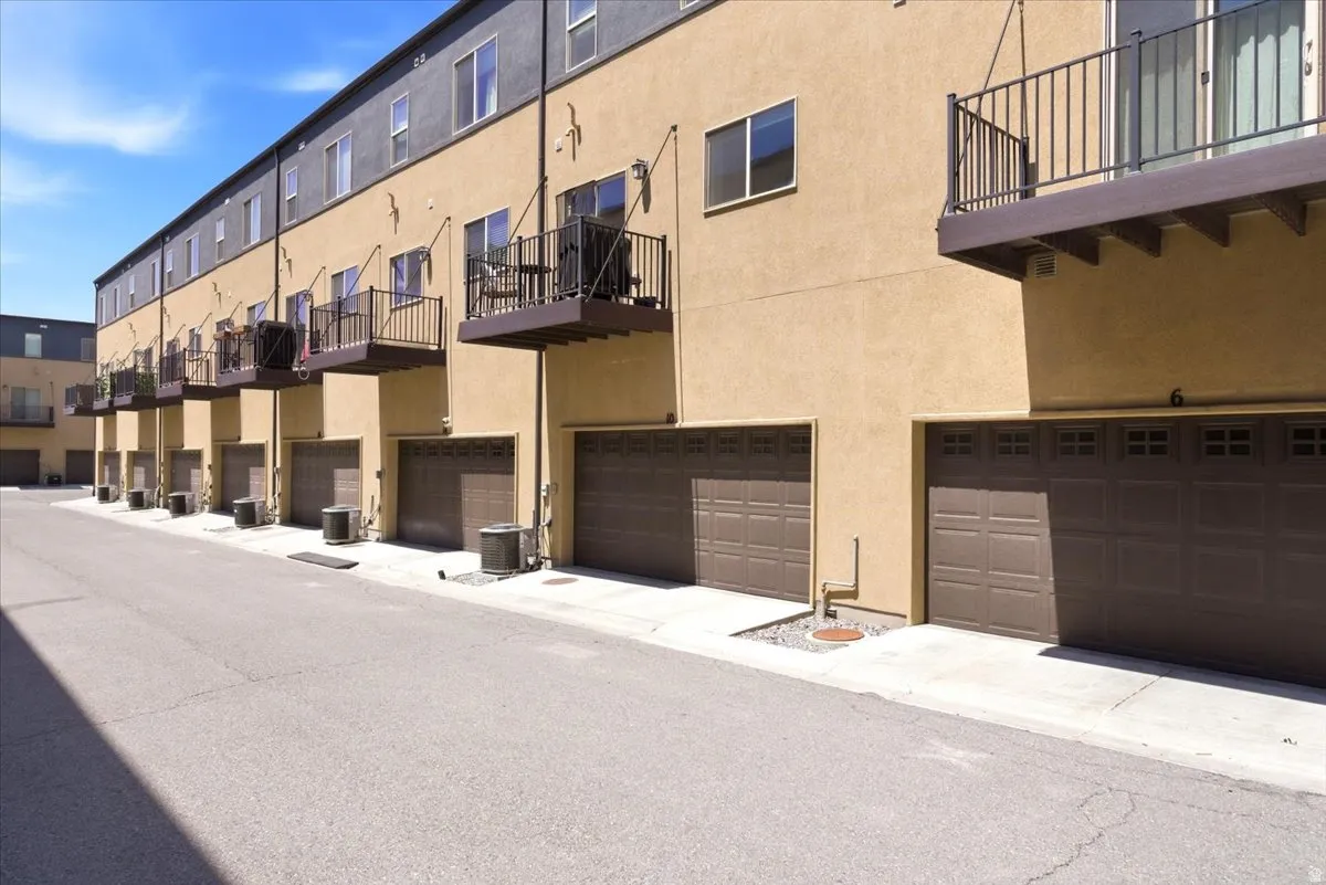 Multi-story stucco townhome exterior featuring individual garages with panel-style doors and upper-level balconies with black iron railings
