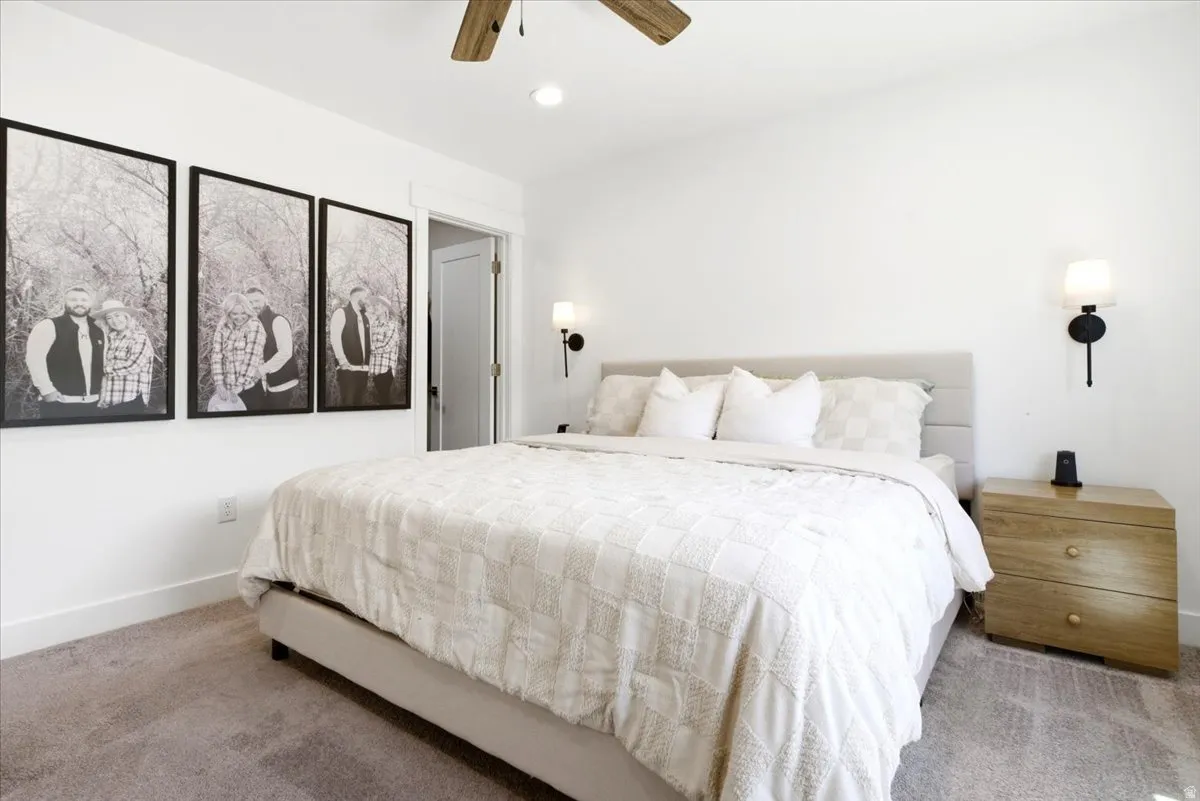 Spacious bedroom featuring light gray carpeting, a textured upholstered headboard, and a contrasting wood-tone ceiling fan