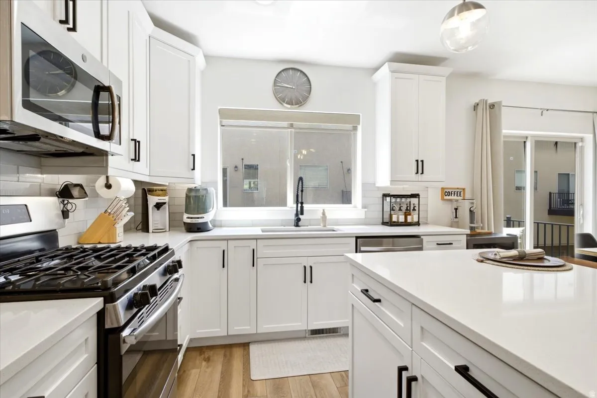 Kitchen featuring white shaker cabinetry, stainless steel appliances, quartz countertops, and wood-finish flooring