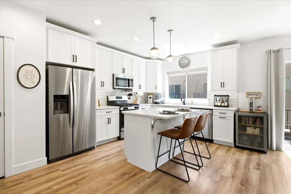 Bright kitchen featuring white cabinetry, stainless steel appliances, a center island with seating, pendant lighting, and wood-finish flooring
