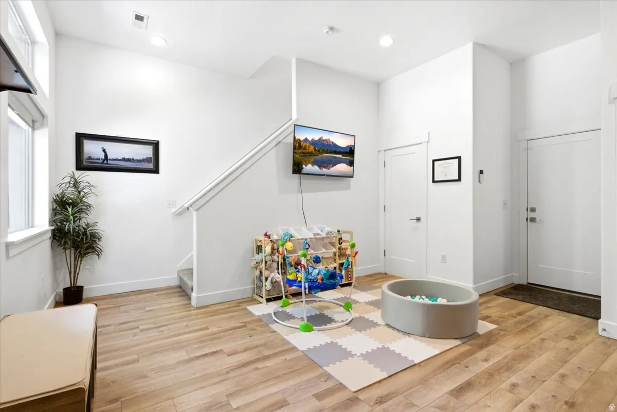 Open-concept entry area featuring light wood-finish flooring, white walls, and a modern white staircase