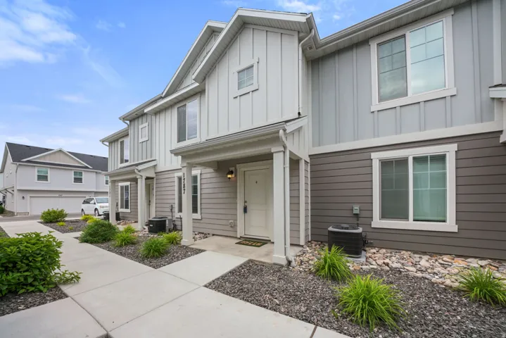 Townhome exterior featuring board and batten siding, horizontal siding, white trim accents, individual covered entryways, and well-maintained landscaping with decorative rock and shrubbery