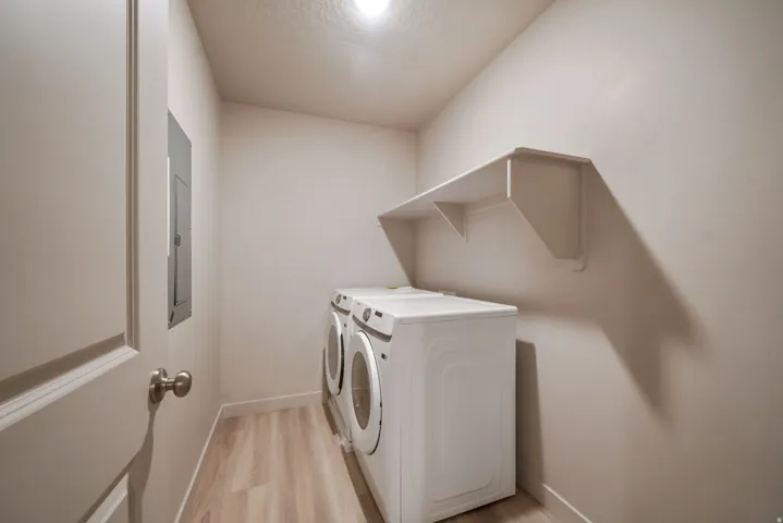 Dedicated laundry area featuring wood-finish flooring, a built-in wall shelf, and a ceiling-mounted light fixture