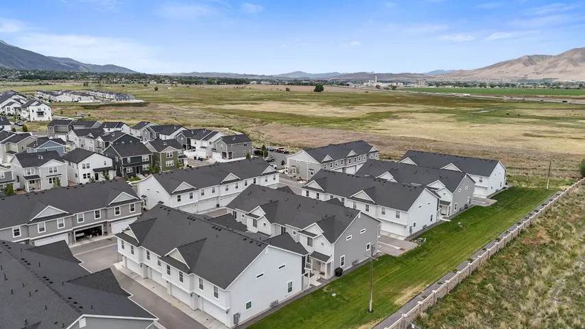 New construction townhomes featuring modern exteriors, dark shingle roofs, attached garages, and a manicured green space