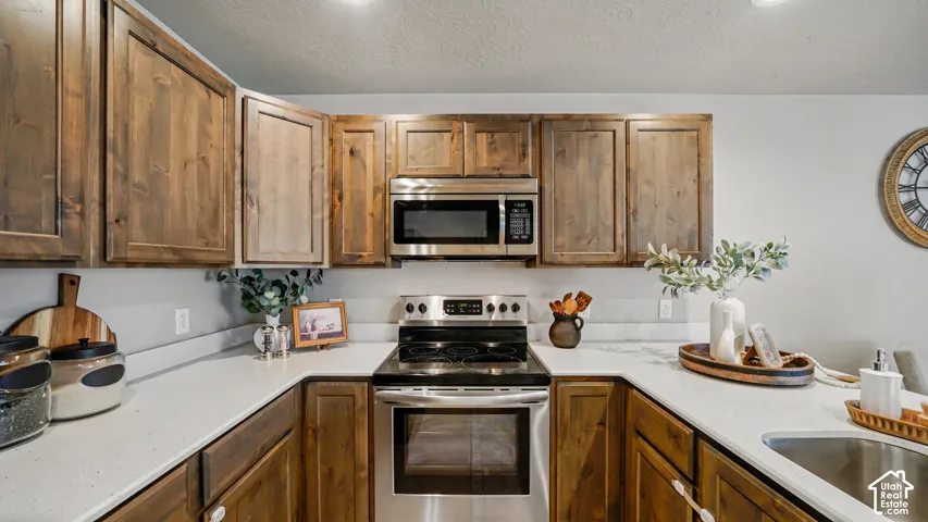 Wood-finish cabinetry, light-colored countertops, stainless steel appliances, and an integrated sink