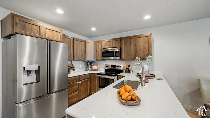 Modern kitchen featuring stainless steel appliances, wood-finish cabinetry, light-toned countertops, and recessed lighting