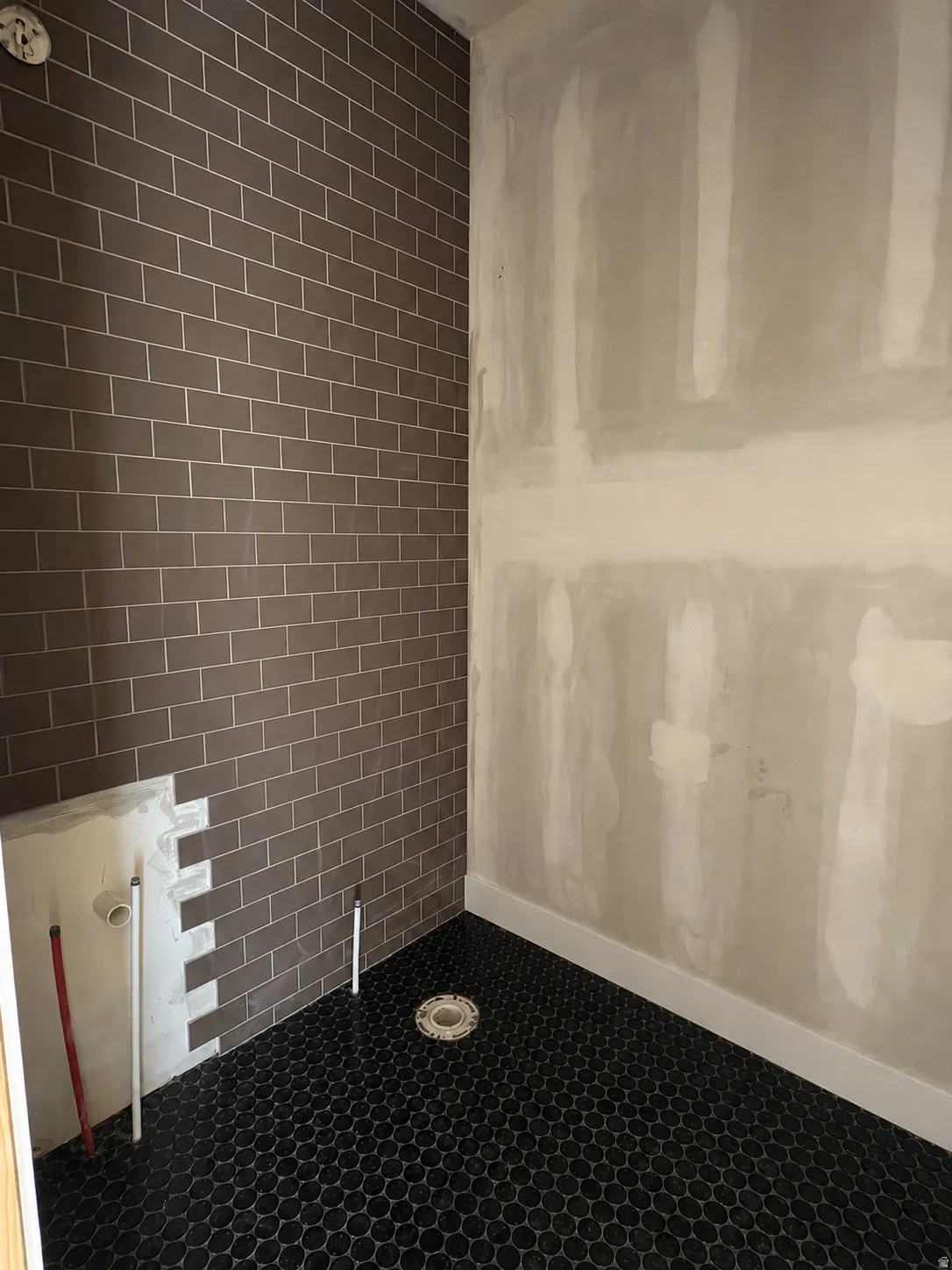 Shower area featuring dark subway tile and a dark penny tile floor
